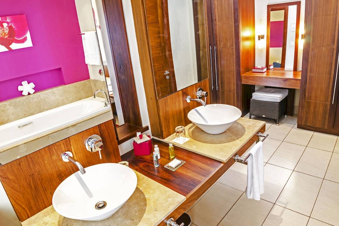 Badezimmer im Tamassa Bel Ombre Hotel mit zwei Waschbecken, einer Badewanne und einer pinken Wand.
