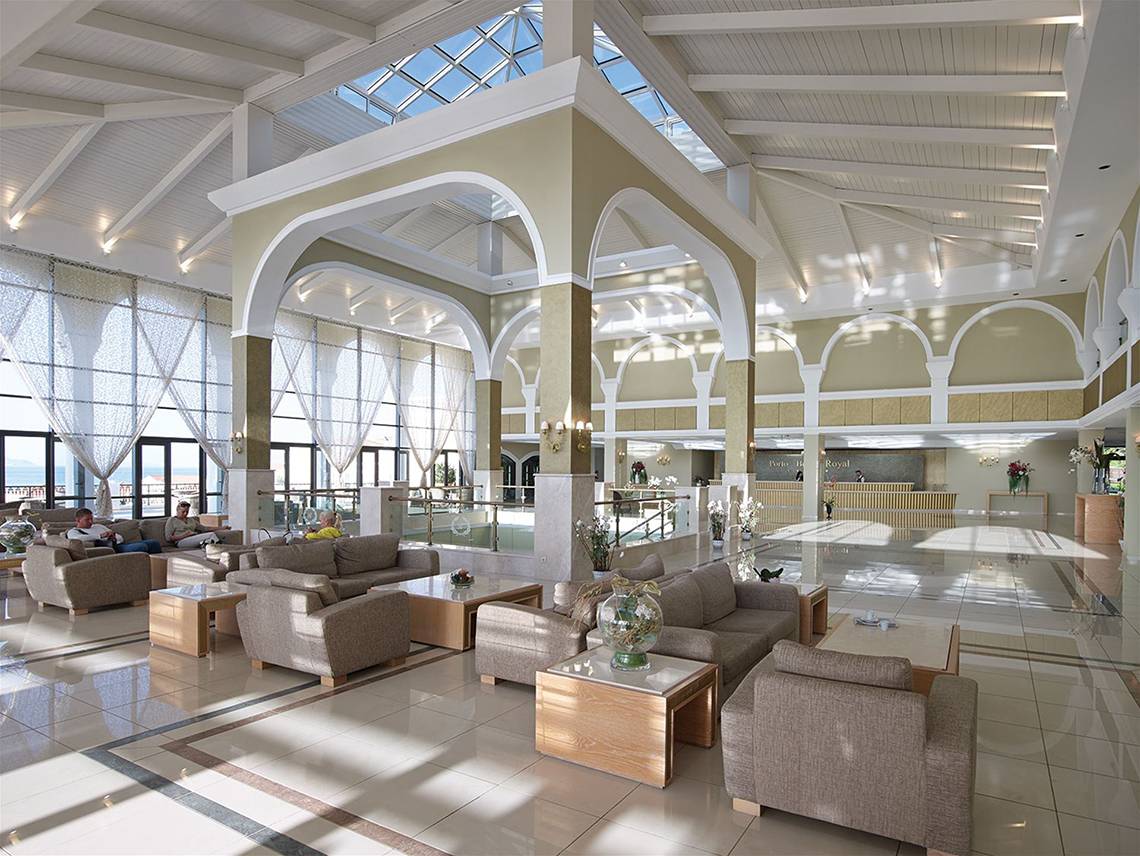 Innenansicht der Lobby des Porto Bello Royal Hotels mit großen Fenstern, heller Beleuchtung und modernen Möbeln.