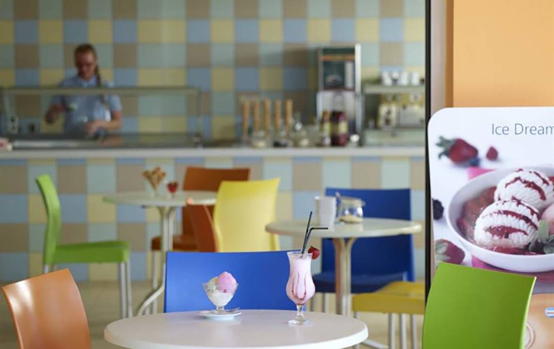 Eisdiele im Porto Bello Royal Hotel mit verschiedenen Eissorten und bunten Stühlen.
