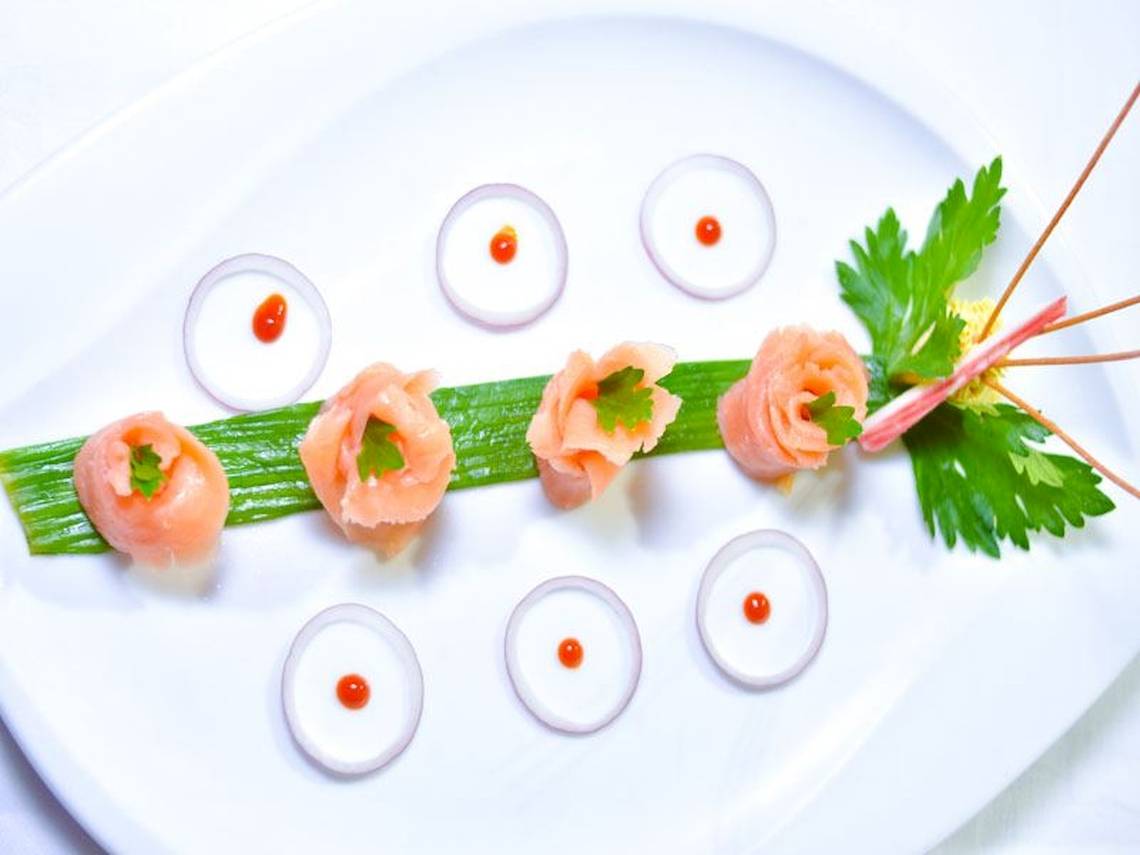 Fünf Stück roher Lachs auf einem Teller mit Zwiebelringen und Blattdekor