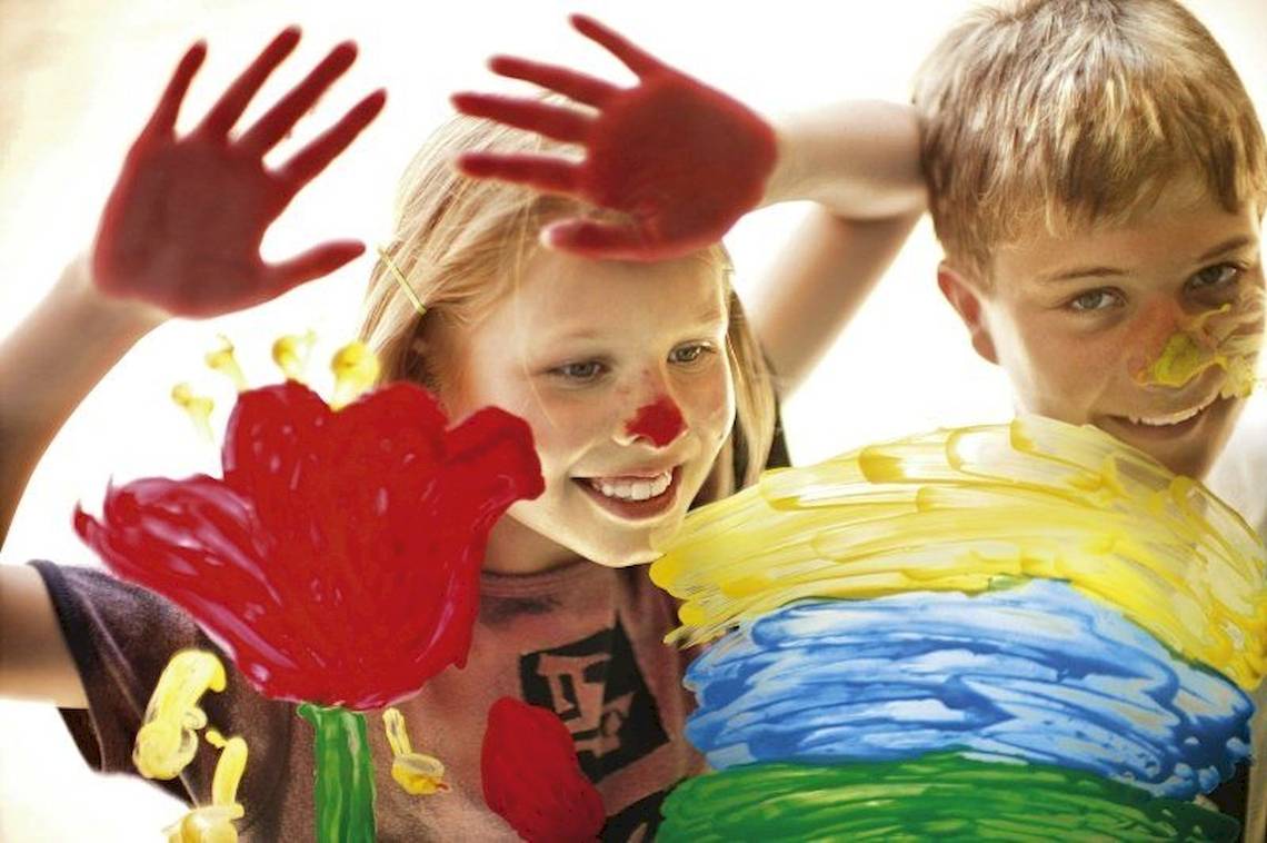 Zwei Kinder mit gemalten Händen und Gesichtern, eines hält eine rote Blume