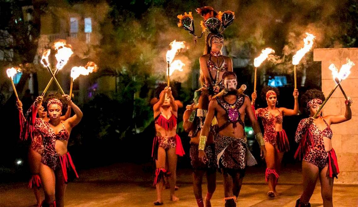 Gruppe von Tänzern in exotischen Kostümen führt eine Feuershow bei Nacht im Playabachata Spa Resort auf.