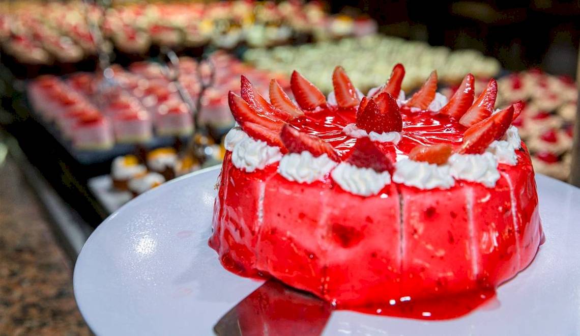 Ein roter Erdbeerkuchen auf einem weißen Teller im Hintergrund ein Buffet