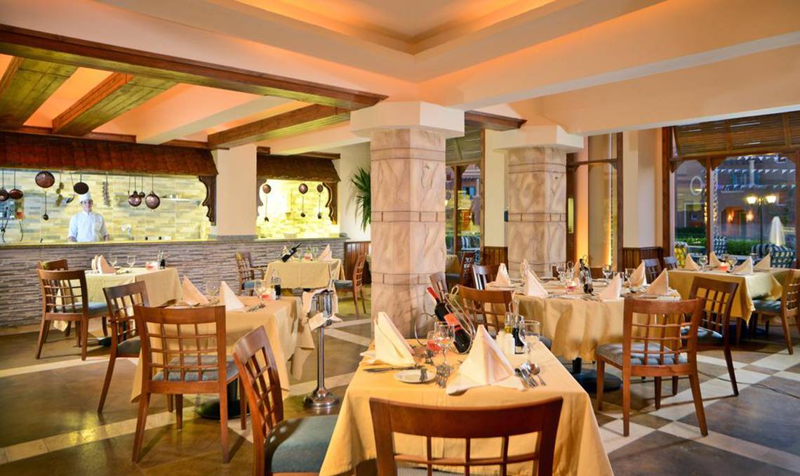 Innenansicht des Restaurants im Charmillion Club Aqua Park mit gedeckten Tischen und einem Koch hinter der Theke.