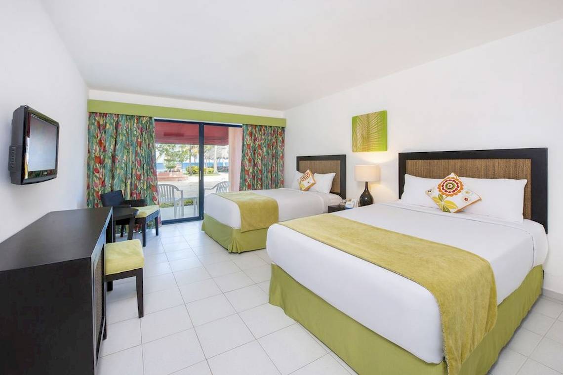Zwei Betten in einem Zimmer des Casa Marina Beach Resort mit grünen Vorhängen und einem Fernseher.