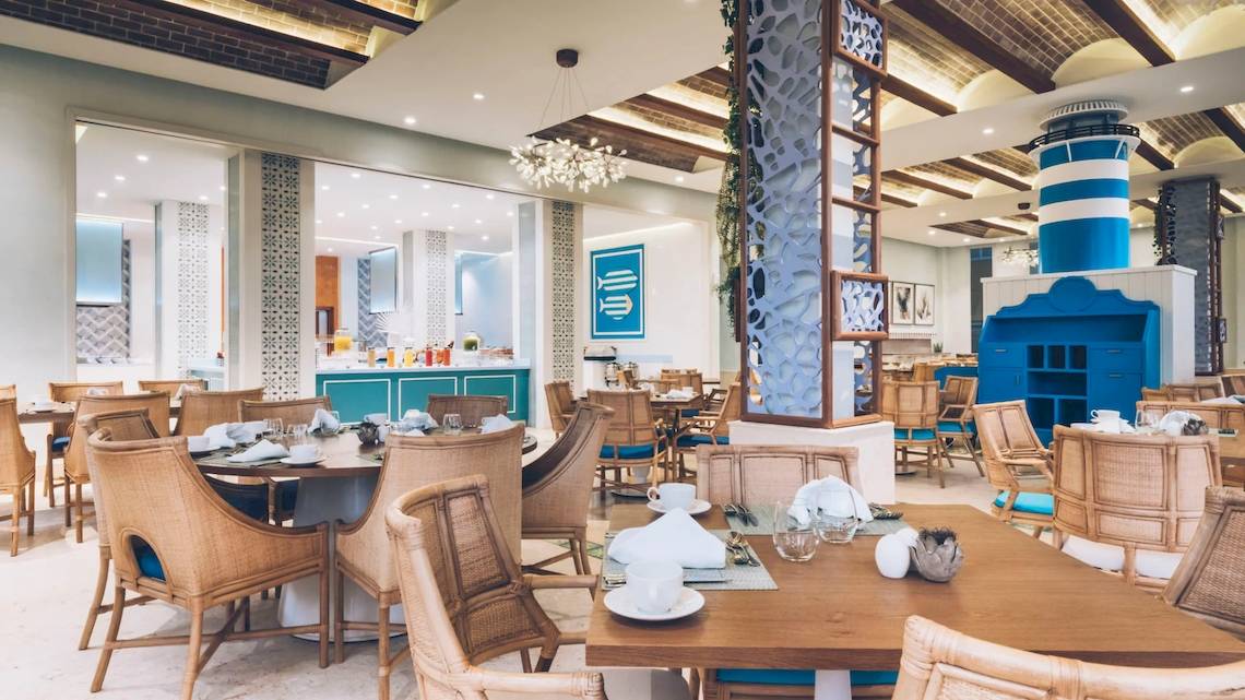 Restaurant-Innenbereich im Coral Level at Iberostar Selection Bávaro mit blauen und weißen Dekorelementen, Holztischen und Stühlen.