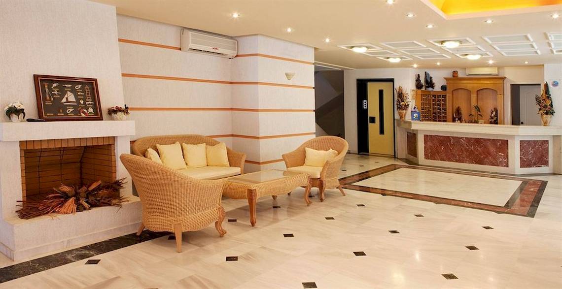 Lobby des Dedalos Beach Hotels mit Kamin, Sofas und Rezeptionstresen.