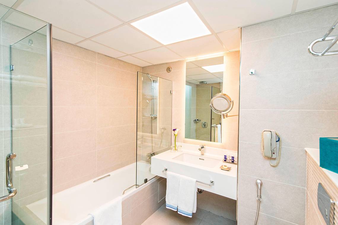 Badezimmer im Habtoor Grand Resort & Spa mit Badewanne, Dusche, Spiegel und Toilettenartikeln