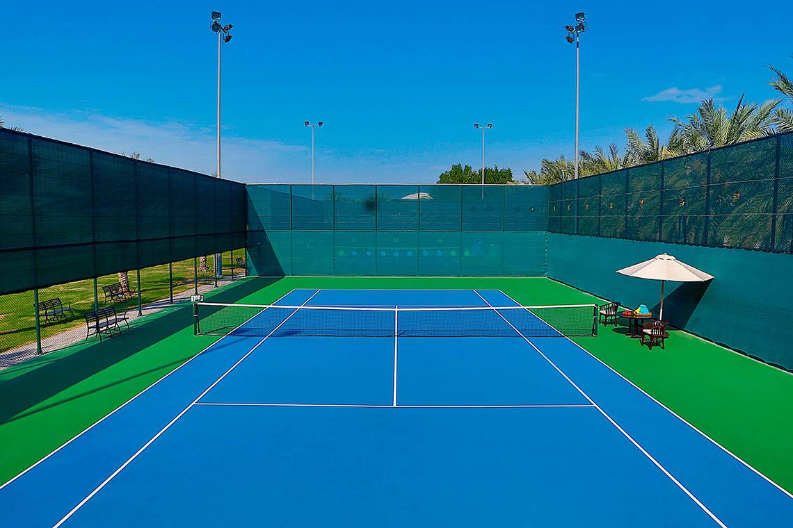 Tennisplatz im Habtoor Grand Resort & Spa mit blauer und grüner Begrenzung und einer Sonnenschirm.