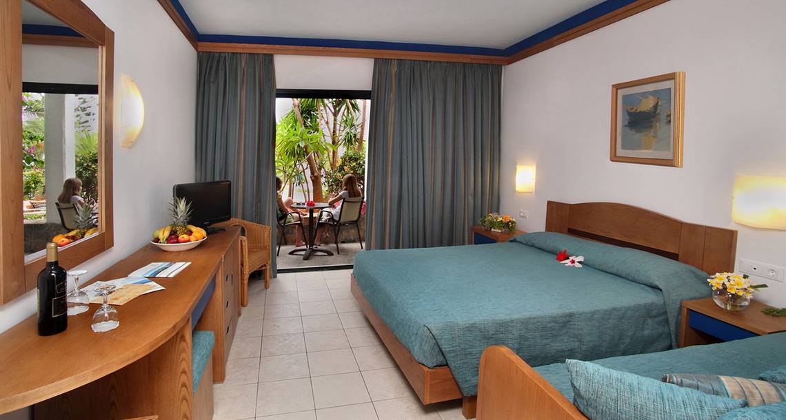Hotelzimmer mit zwei Betten, Balkon, Fernseher, und Obst auf dem Schreibtisch.