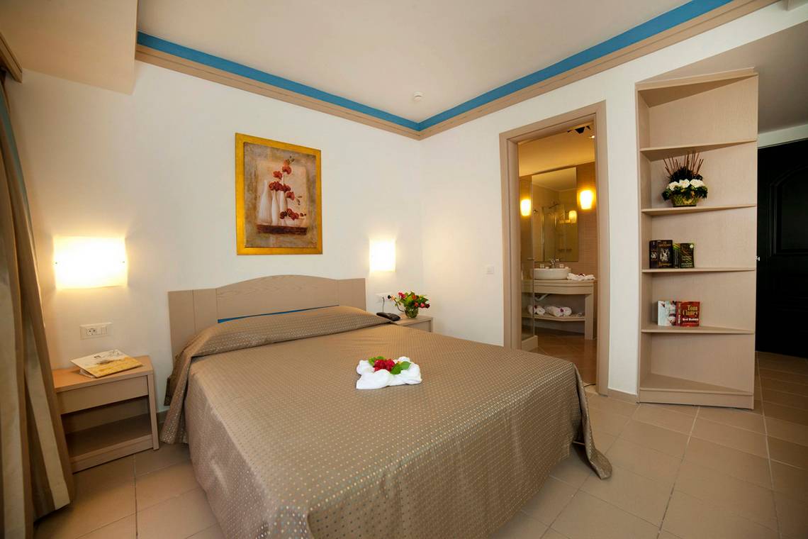 Hotelzimmer des Nana Golden Beach mit Bett, Nachttisch, Kunstwerk und Badezimmereingang.