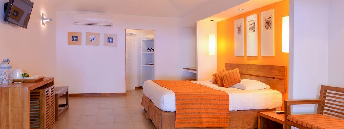 Innenansicht eines Hotelzimmers im Adaaran Select Hudhuran Fushi, mit Bett, Fernseher und Möbeln.