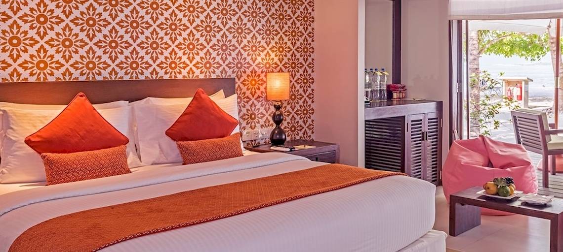 Hotelzimmer im Adaaran Select Hudhuran Fushi mit einem Bett, Kissen, Tisch, Lampe und einem Blick auf den Garten.