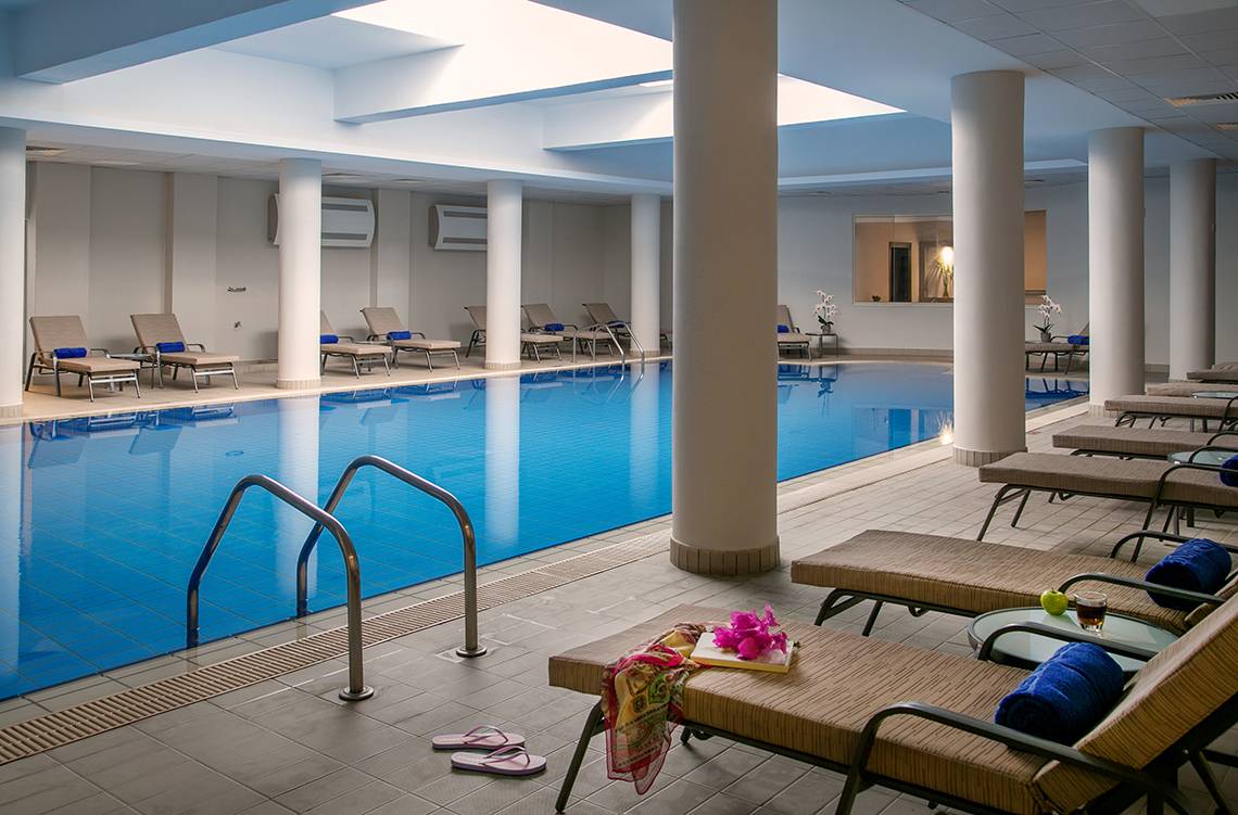 Innenpool des Louis Paphos Breeze Hotels mit Lounge-Liegestühlen und Dekoration.