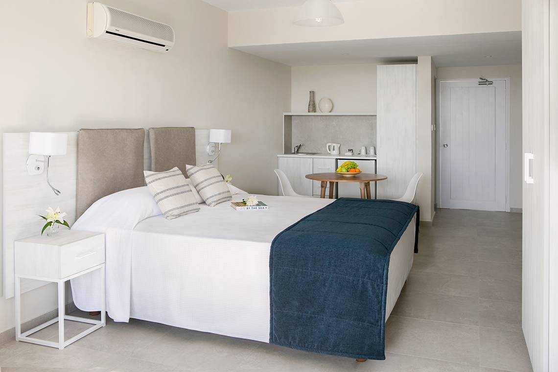 Innenansicht eines Zimmers im Louis Paphos Breeze Hotel mit einem Bett, Tisch, und einer kleinen Küche.