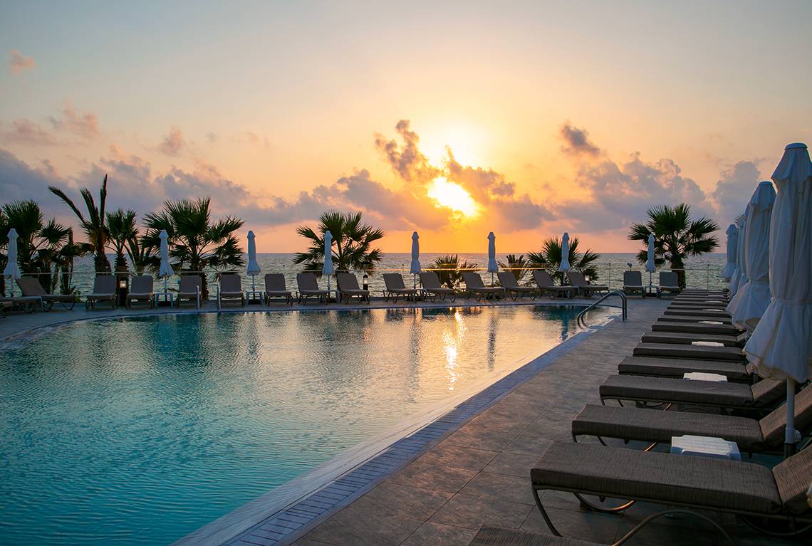Sonnenuntergang am Pool des Louis Paphos Breeze Hotels mit Loungestühlen und Palmen