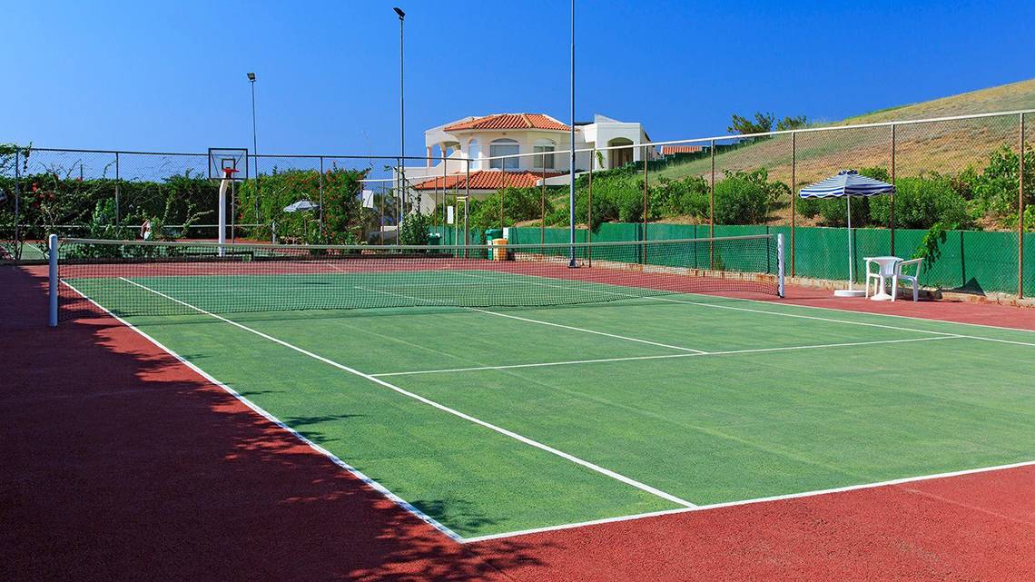 Tennisplatz vor dem Hotel Rodos Princess Beach mit einem Basketballkorb und einem Tisch mit Sonnenschirm.