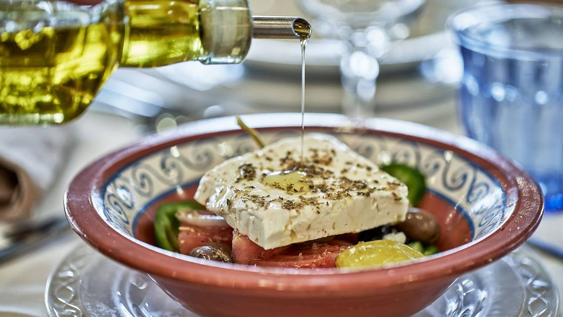 Olivenöl wird auf einen griechischen Salat in einer Schüssel gegossen.