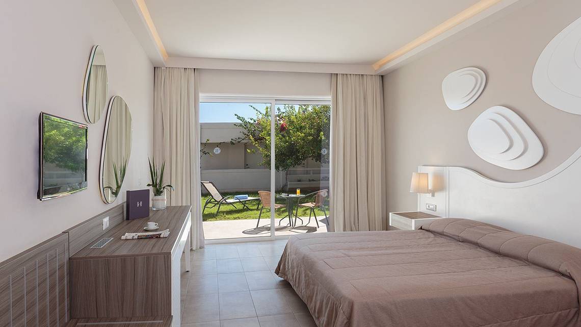 Innenansicht eines Hotelzimmers im Rodos Princess Beach Hotel mit Bett, Fernseher und Balkon.