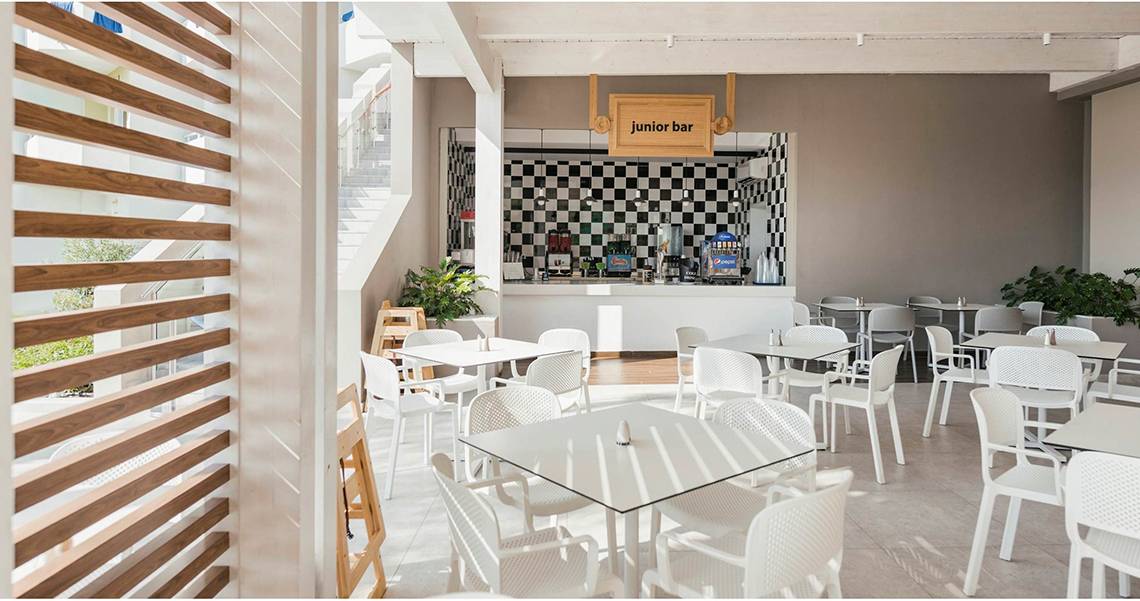 Innenansicht des Junior Bars im Esperides Beach Resort mit weißen Tischen und Stühlen.