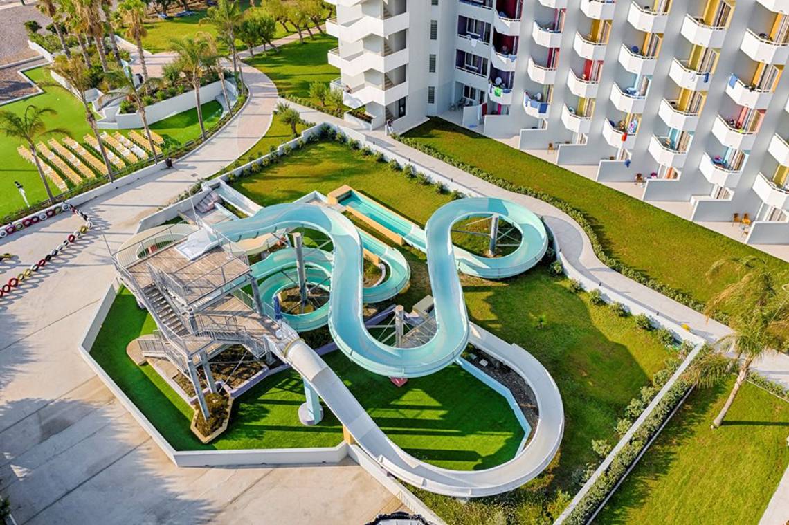Luftaufnahme der Wasserrutsche im Esperides Beach Resort mit einem Schwimmbecken und mehreren Gebäuden im Hintergrund.