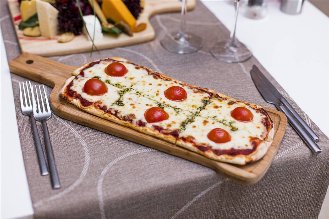 Eine Pizza auf einem Holzbrett mit Tomaten und Käse, serviert auf einem Tisch mit Silberbesteck.