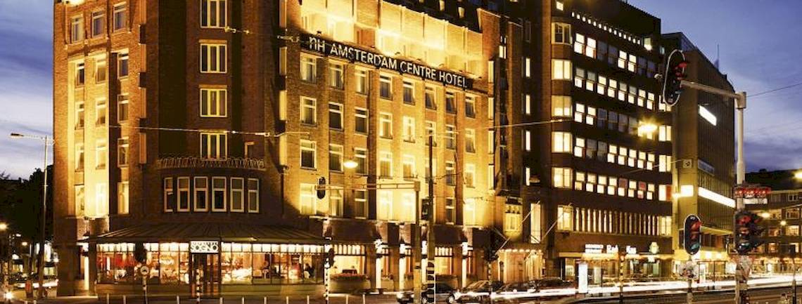 Das NH Amsterdam Centre Hotel ist nachts beleuchtet und steht an einer belebten Straße.