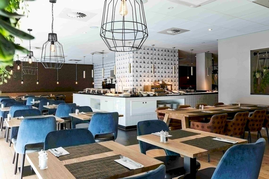 Innenansicht des Restaurants des NH Amsterdam Centre Hotels mit blauen Stühlen und Tischen.