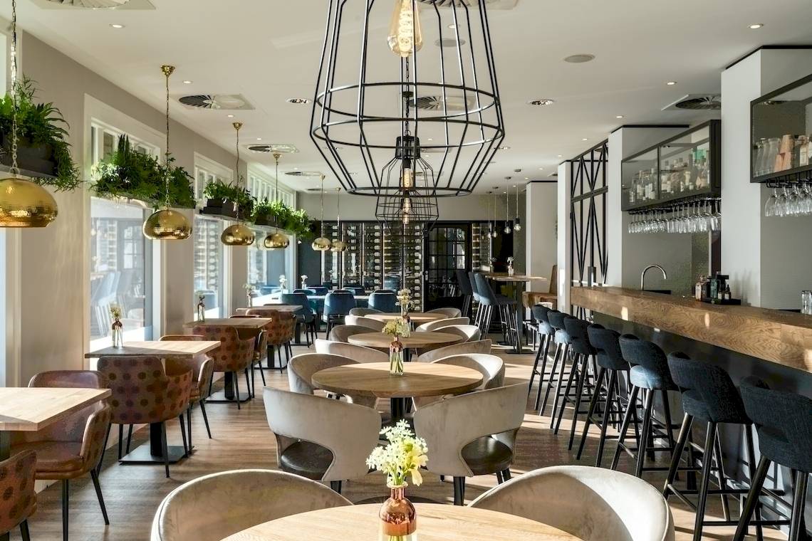 Innenansicht des NH Amsterdam Centre Restaurants mit Tischen, Stühlen und einer Theke.