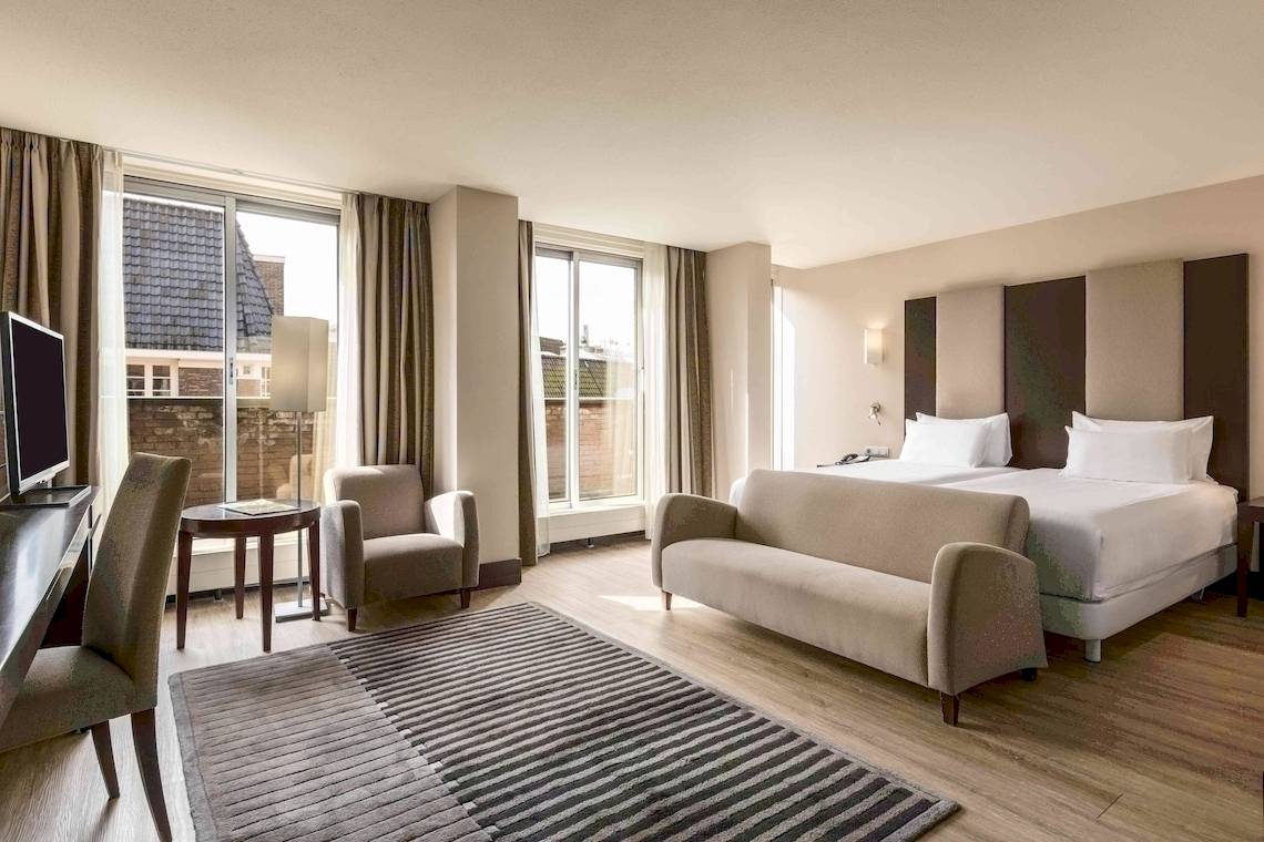 Schlafzimmer im NH Amsterdam Centre Hotel mit Doppelbett, Sofa, Schreibtisch und Fenstern