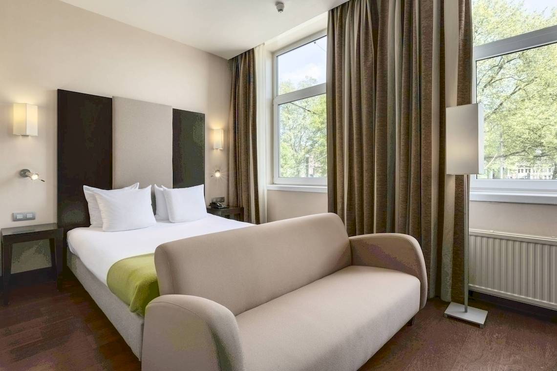 Ein Zimmer im NH Amsterdam Centre Hotel mit einem Bett, einer Couch und Fenstern.