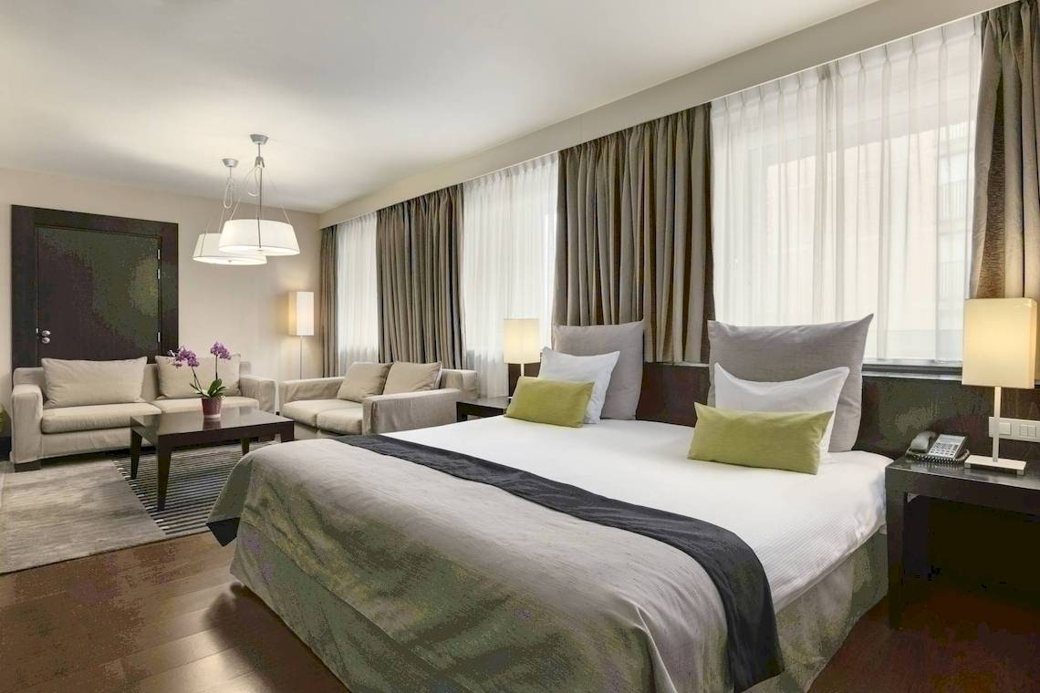 Schlafzimmer im NH Amsterdam Centre Hotel mit großem Bett, Sofas und Nachttischen.