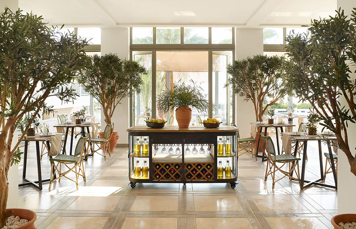 Innenbereich des Restaurants im Grecotel Lux Me Dama Dama mit großen Bäumen, Tischen und Stühlen.