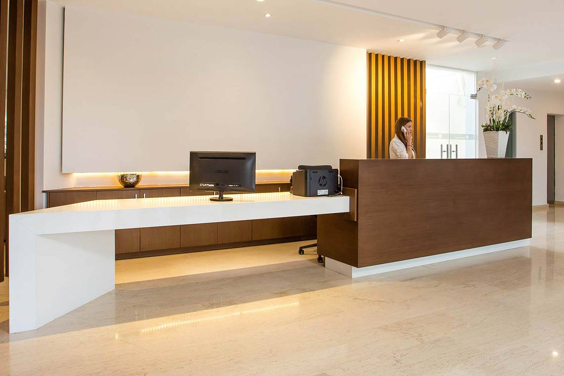Empfangsbereich des Niriides Beach Hotels mit weißer Theke und einer Dame am Telefon.
