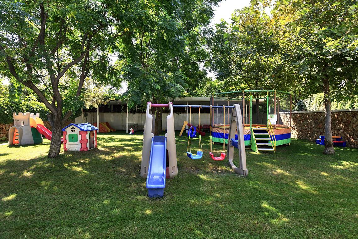 Ein Kinderspielplatz im Freien im Su Hotel mit Rutschen, Schaukeln und Klettergerüst.