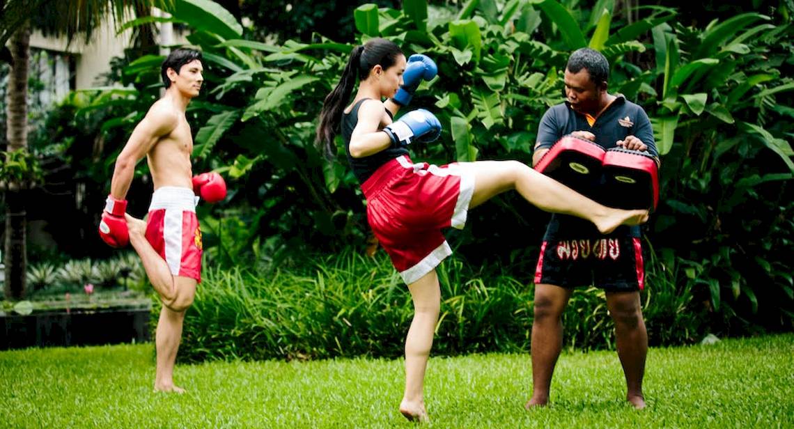 Drei Personen machen Muay Thai Training im Freien, einer kickt während zwei andere zuschauen.