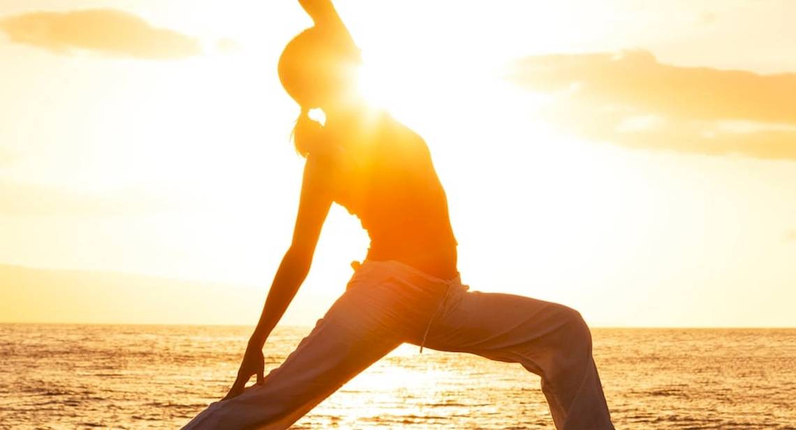 Person praktiziert Yoga am Strand bei Sonnenaufgang mit Blick auf das Meer