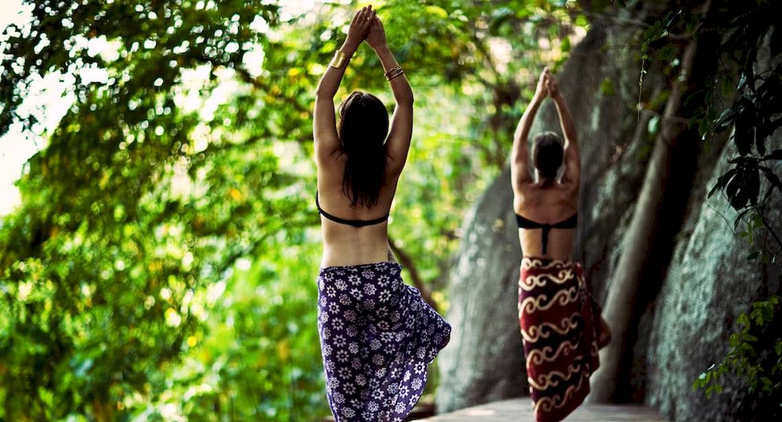 Zwei Frauen praktizieren Yoga in einem Wald bei Anantara Rasananda Koh Phangan Villas.