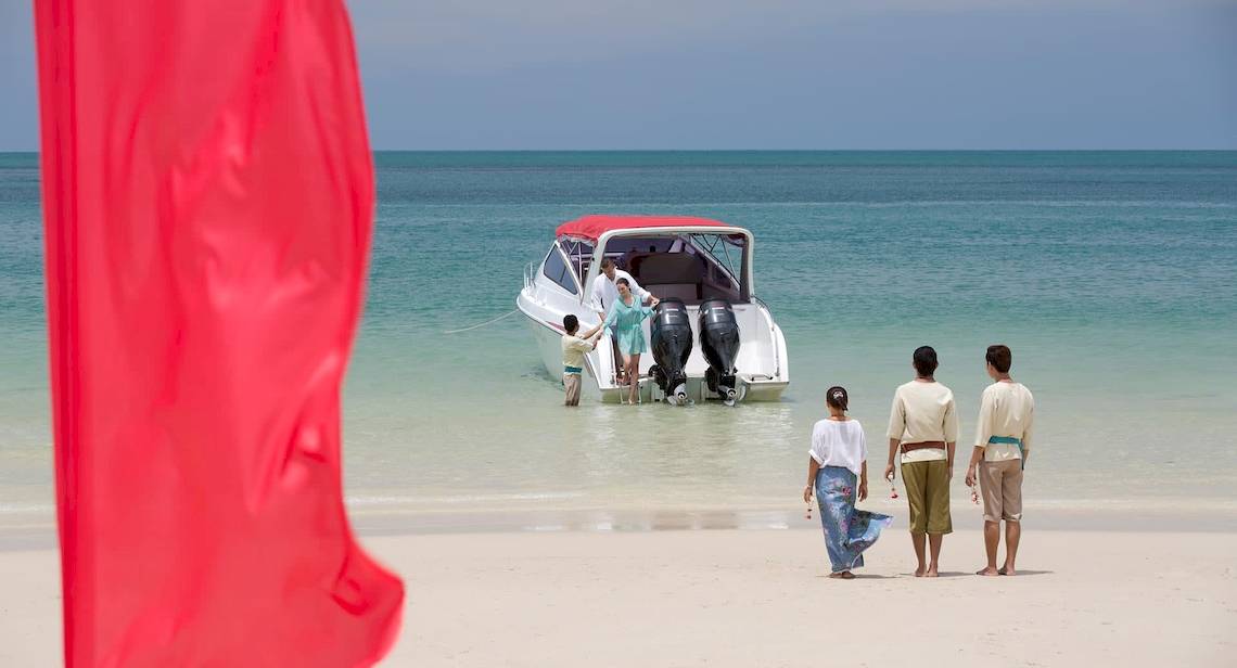 Familie am Strand von Anantara Rasananda Koh Phangan Villas mit einem Boot im Hintergrund