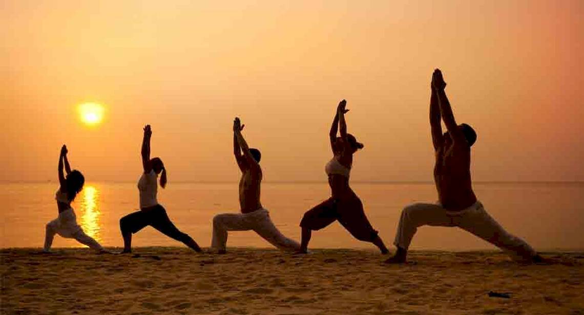 Mehrere Personen praktizieren Yoga auf dem Strand bei Sonnenuntergang.