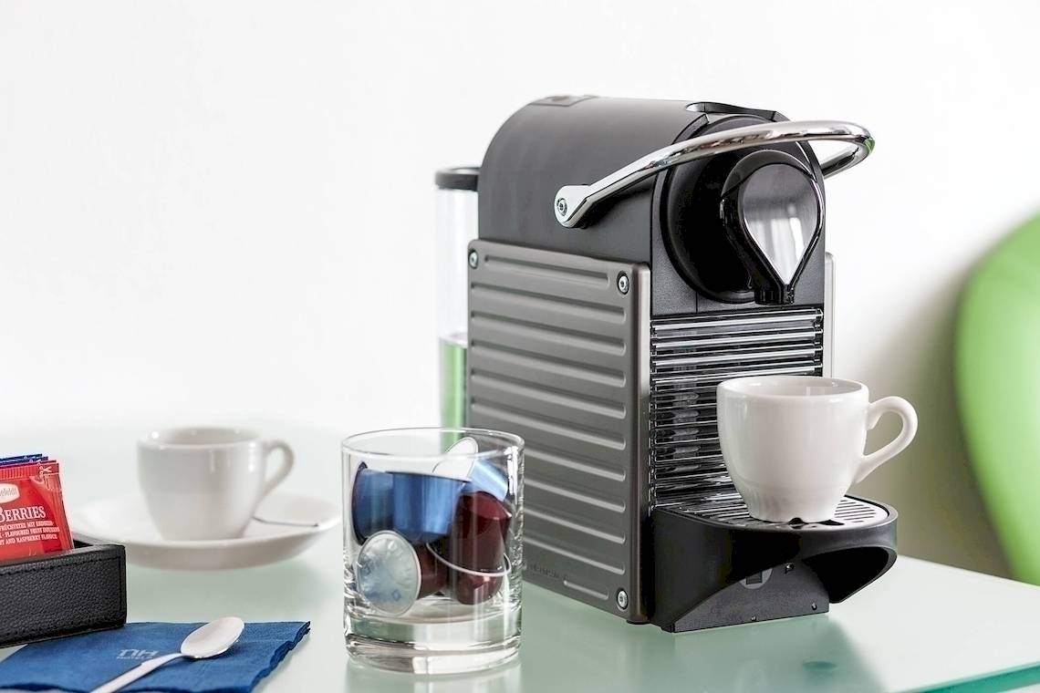 Kaffeemaschine des NH Hamburg Altona auf einem Tisch mit Tassen und Kaffeekapseln.