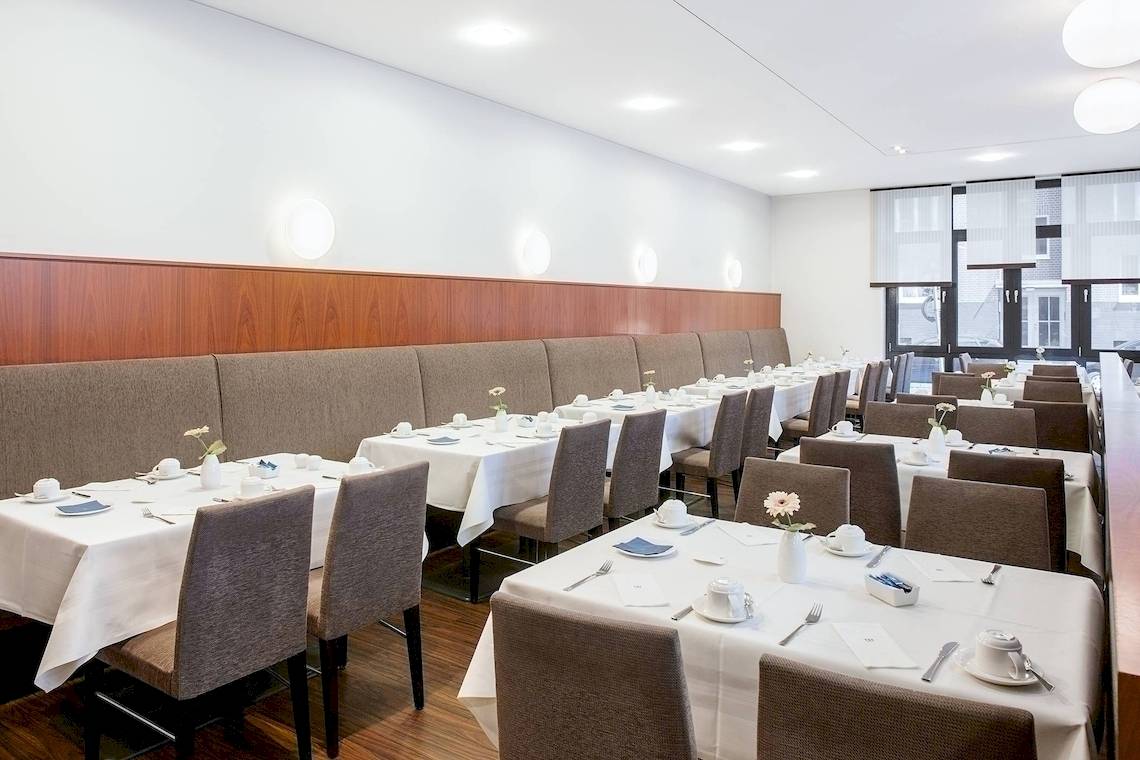 Innenansicht des Restaurants im NH Hamburg Altona Hotel mit gedeckten Tischen und dekorativen Blumenarrangements.