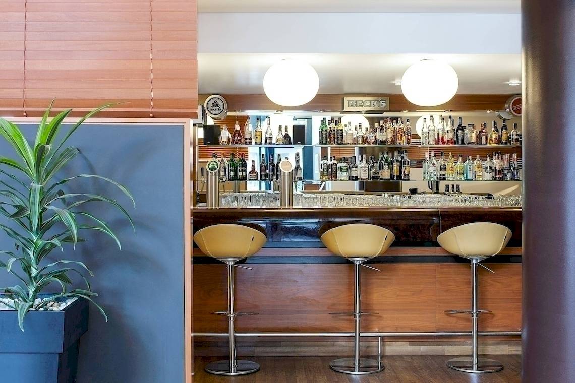 Die Bar im NH Hamburg Altona Hotel mit runden Barhockern und einer grünen Pflanze.
