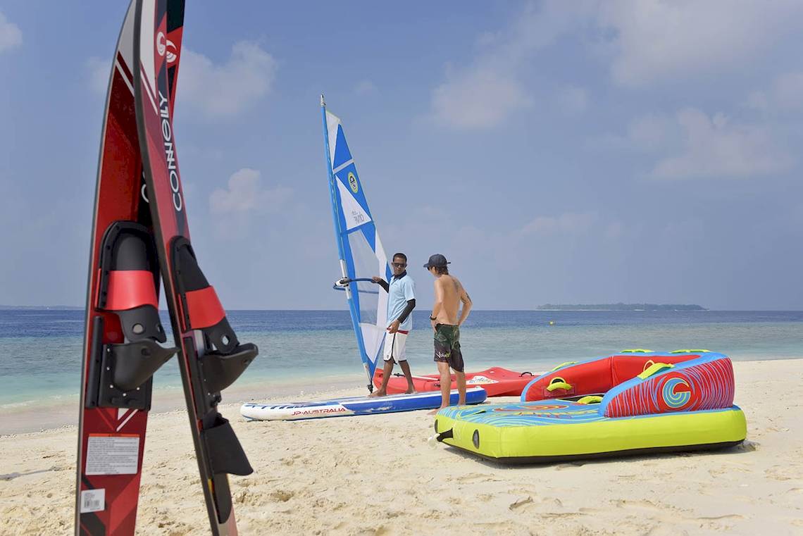 Zwei Männer stehen am Strand neben Wassersportgeräten und einer Segelsurfanlage.