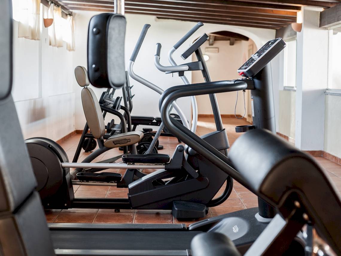 Fitnessbereich im Colonna Grand Hotel Capo Testa mit mehreren Geräten wie Laufbändern und Rudergeräten.