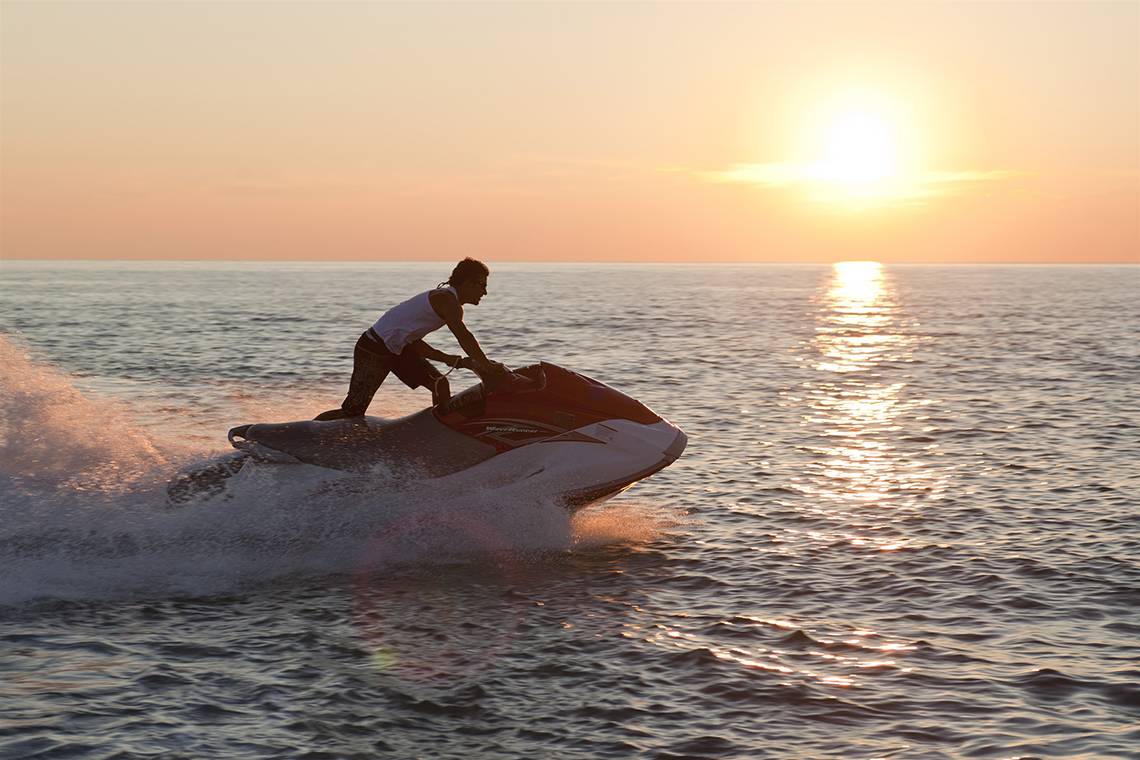 Mann auf Jet Ski bei Sonnenuntergang auf dem Meer