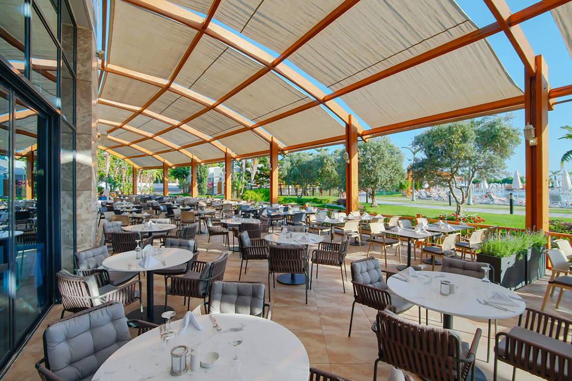 Terrasse des Baia Lara Hotels mit vielen Tischen und Stühlen unter einem Sonnensegel.