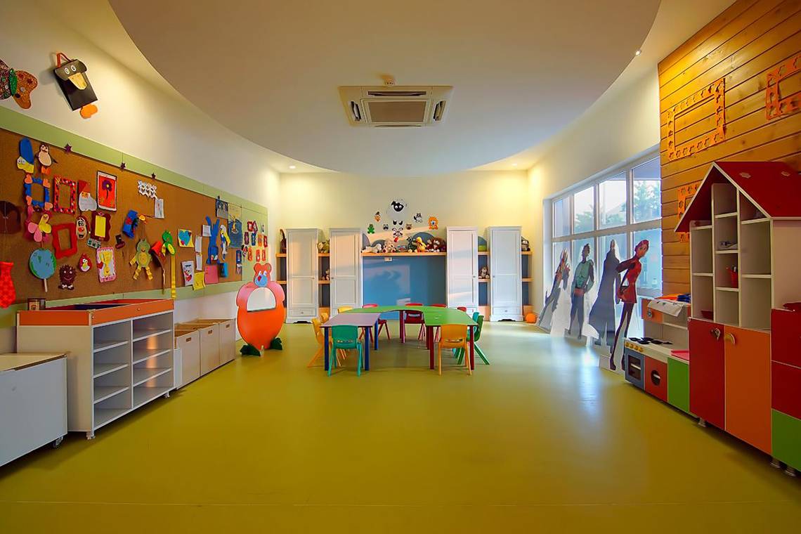 Das farbenfrohe Kinderzimmer im Baia Lara Hotel mit runden Tisch, bunten Stühlen und dekorativen Wandtafeln.