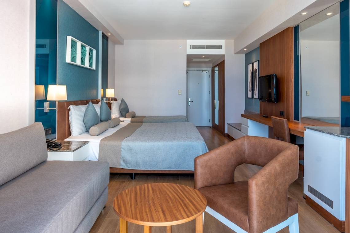Innenansicht eines Zimmers im Baia Lara Hotel mit zwei Betten, einem Schreibtisch, einem Fernseher und Möbeln.