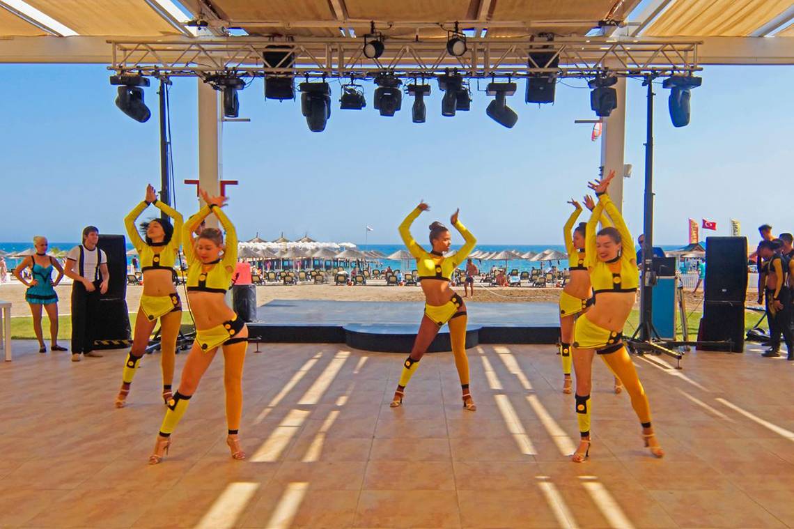 Tanzgruppe in gelben Outfits auf einer Bühne im Freien am Strand des Baia Lara Hotels.